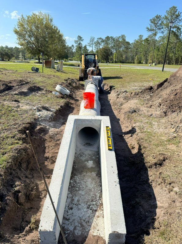 Concrete culvert installation in progress with skid steer and proper drainage grading