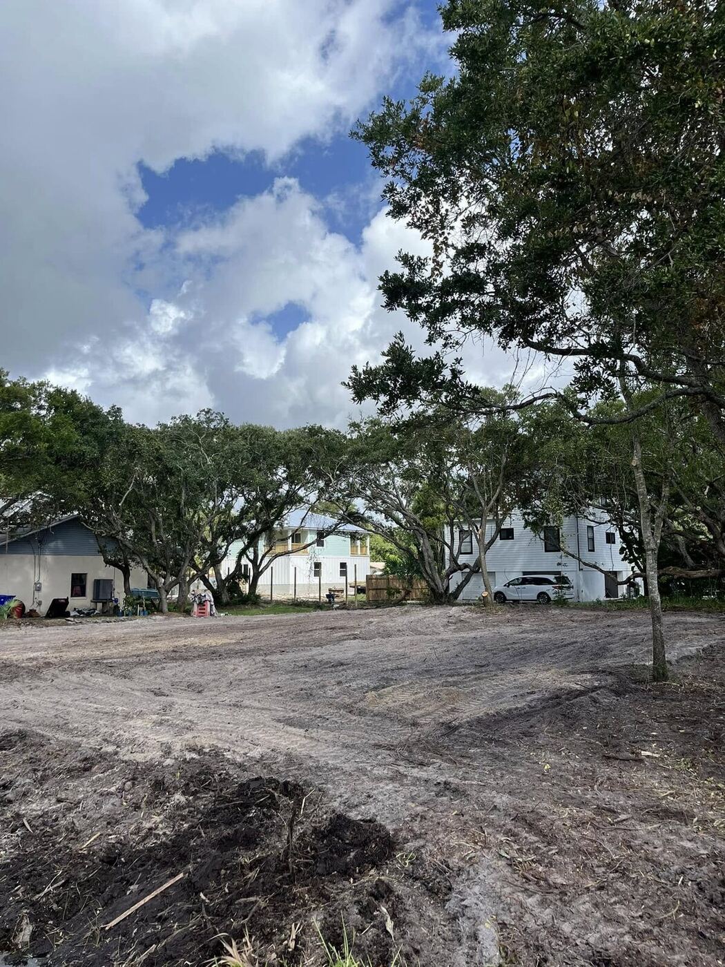 Residential infill lot freshly graded between neighboring homes, with mature live oaks preserved on the property