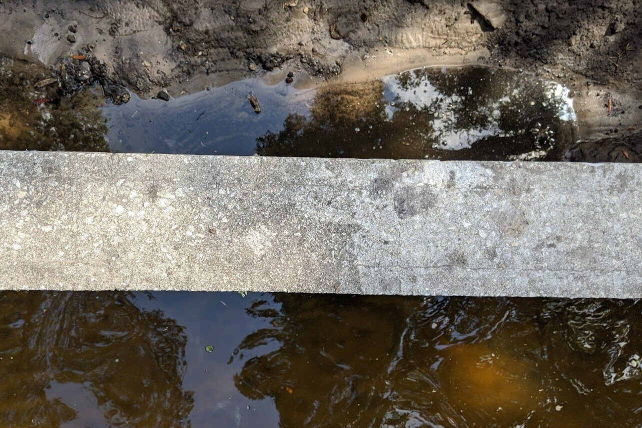 Mid-repair view of the seawall with the failed area fully excavated, exposing the back of the wall with water visible on both sides