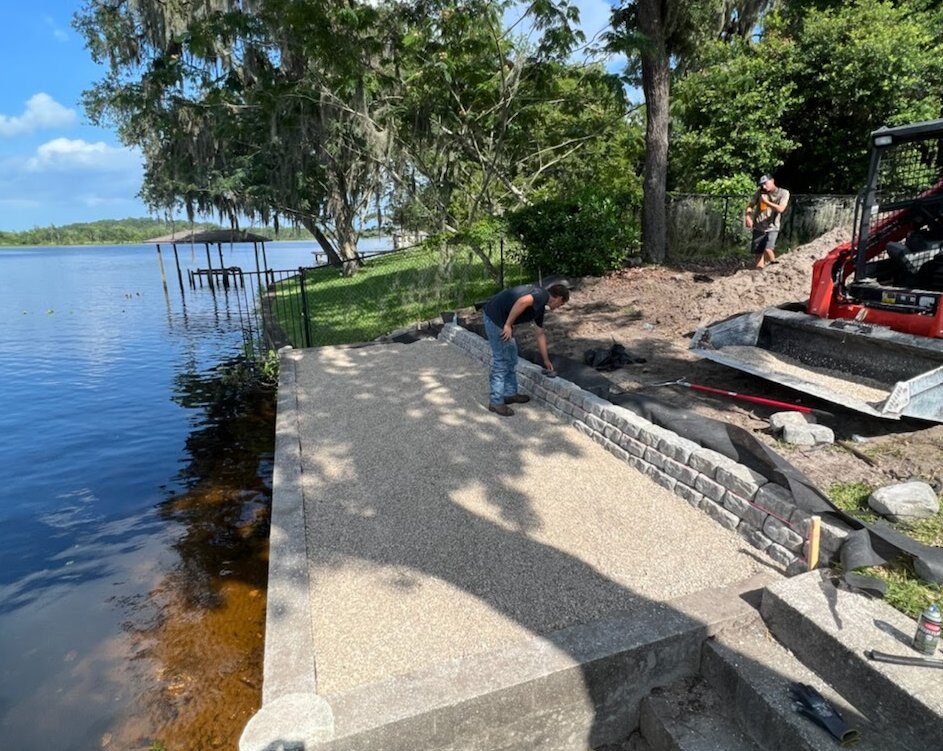Completed seawall repair on the St. Johns River with new exposed-aggregate pad, stone retaining edge, and re-anchored wall