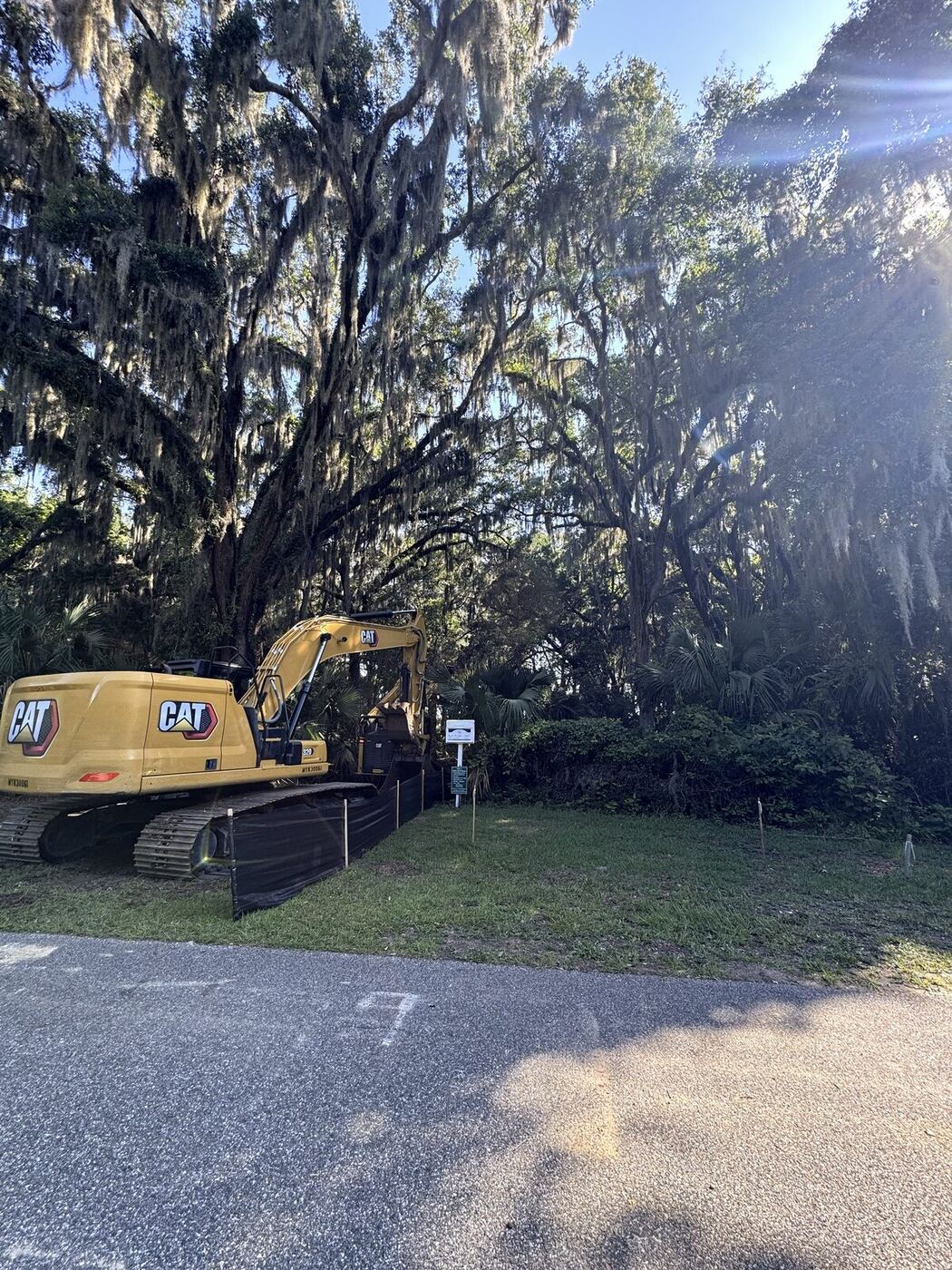 Full-size CAT 320 excavator staged at the wooded waterfront lot with silt fence installed before clearing began