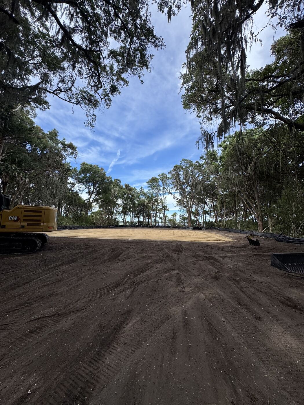 Cleared and graded waterfront lot with a compacted building pad, oak canopy overhead and water visible through the trees, Northeast Florida